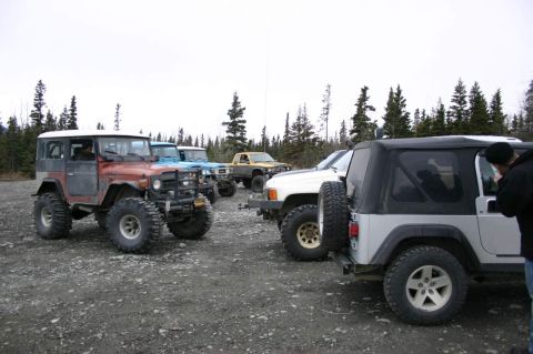 2003 Jeep TJ - A group of off-road vehicles are parked together on a gravel surface with a forest in the background.