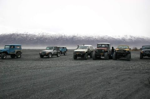 2003 Jeep TJ - A group of off-road vehicles are parked on a gravel surface with mountains in the distance.