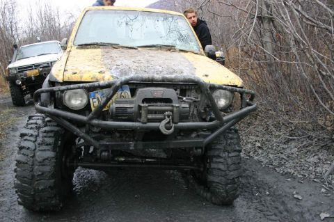 2003 Jeep TJ - Two off-road vehicles are stuck in the mud on a trail surrounded by bare trees and brush.