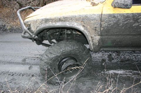 2003 Jeep TJ - This off-road vehicle appears to be stuck deep in mud, with its front tire submerged.