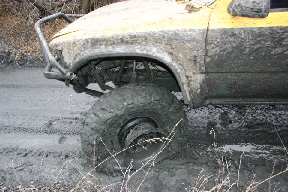 Yellow off-road vehicle with large tires stuck in thick mud, front bumper visible