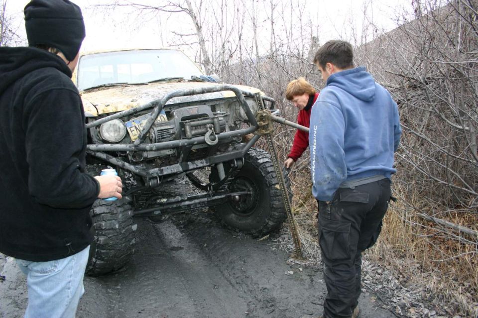 Modified off-road vehicle stuck in mud with three people around it