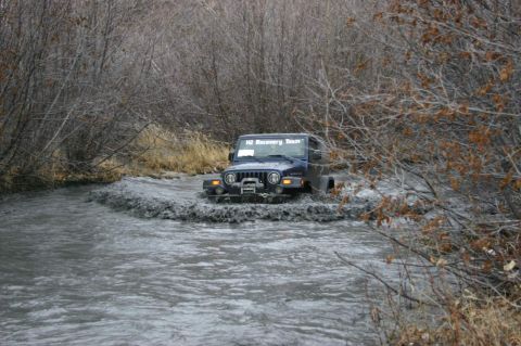 2003 Jeep TJ - A blue 2003 Jeep TJ navigates a muddy stream, with "H2 Recovery Team" visible on its windshield.