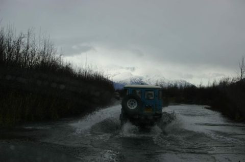 2003 Jeep TJ - Off-roading through water with snowy mountains in the distance.