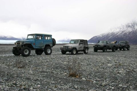 2003 Jeep TJ - A convoy of off-road vehicles traverses a rocky, glacial landscape under an overcast sky.