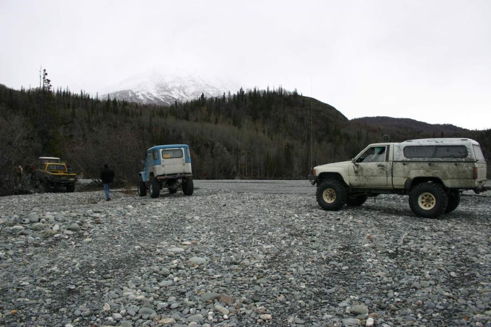 White pickup truck with a camper shell, lifted suspension, and large tires on a rocky terrain