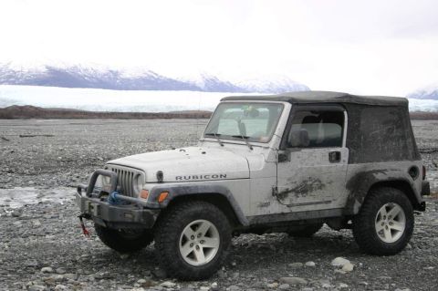 2003 Jeep TJ - A silver 2003 Jeep TJ Rubicon is parked on a rocky shore, with a glacier and snow-capped mountains visible in the distance.