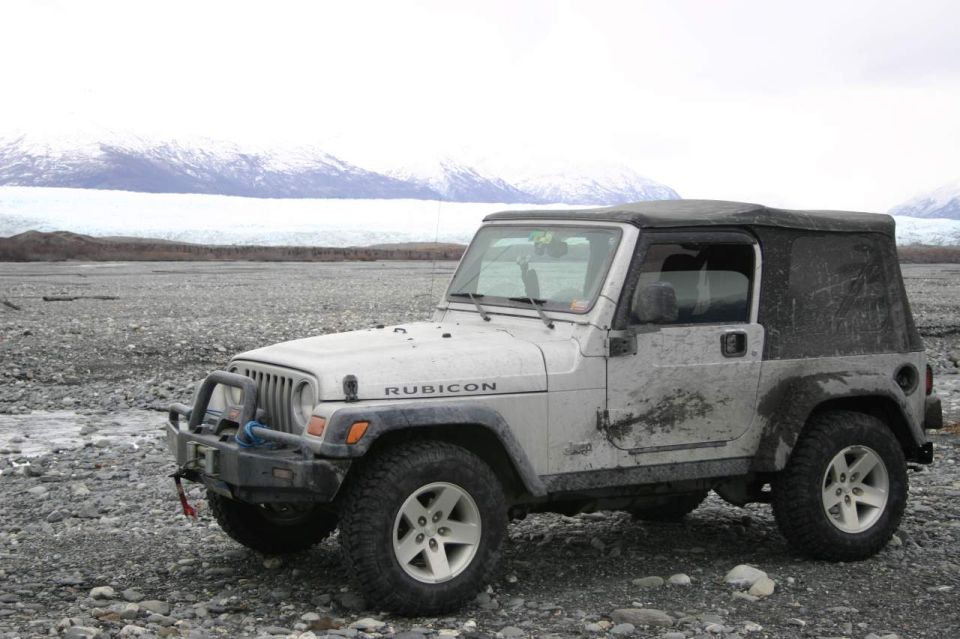 Silver 2003 Jeep TJ Rubicon with a black soft top parked on a rocky shore with a glacier in the background