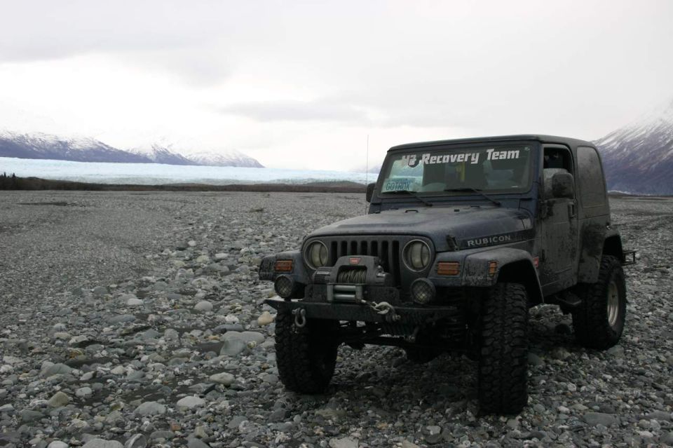 Dark blue 2003 Jeep TJ Rubicon parked on a rocky shore with a glacier and mountains in the background. "M3 Recovery Team" sticker on windshield