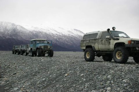 2003 Jeep TJ - A convoy of 4x4s traverses a desolate, rocky terrain under a cloudy sky with distant snow-covered peaks.