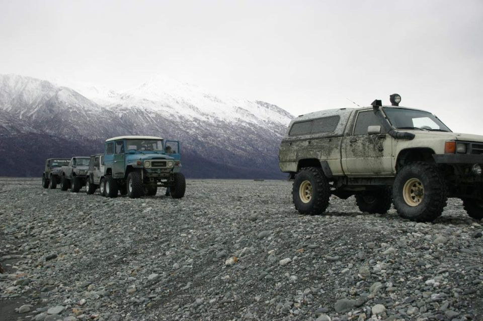 Several off-road vehicles lined up on a rocky plain with snow-capped mountains in the background