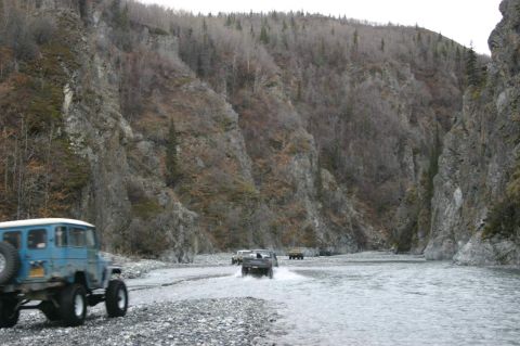 2003 Jeep TJ - Several off-road vehicles navigate a shallow river through a rocky canyon.