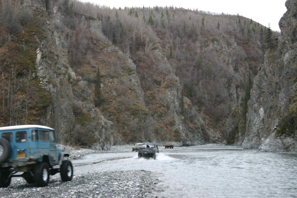 Blue off-road vehicle with spare tire on rear, driving on rocky riverbed