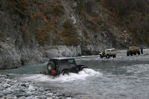 2003 Jeep TJ - Multiple off-road vehicles navigate a rocky riverbed in a mountainous area.