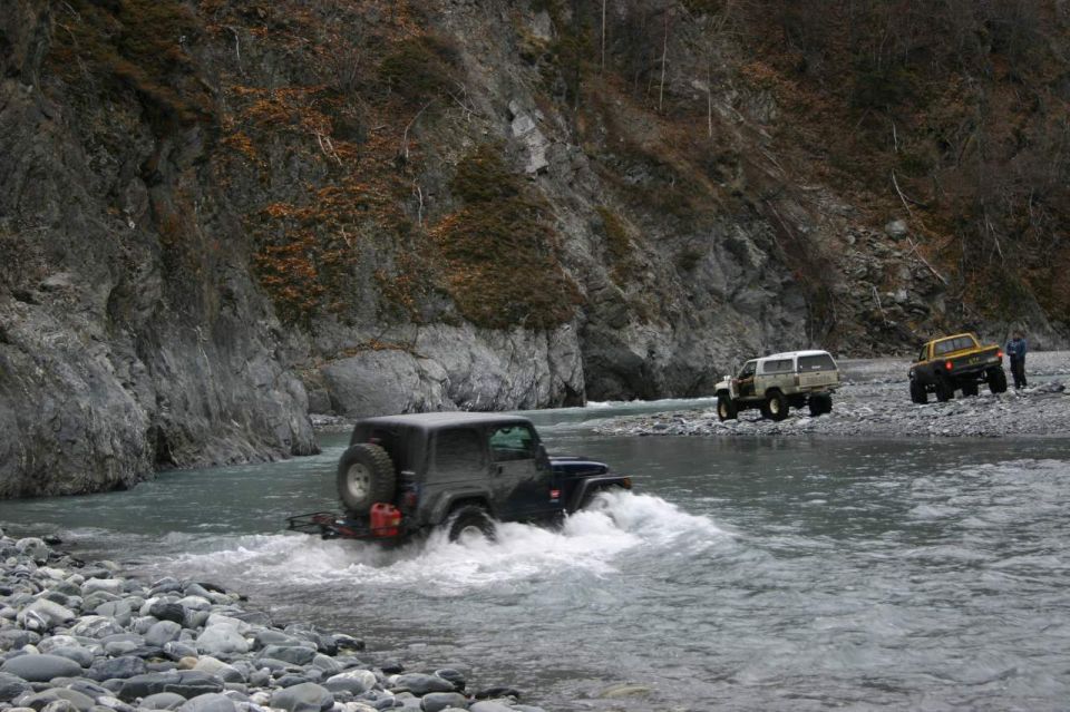 Black 2003 Jeep TJ crossing a shallow river with two other vehicles in the background
