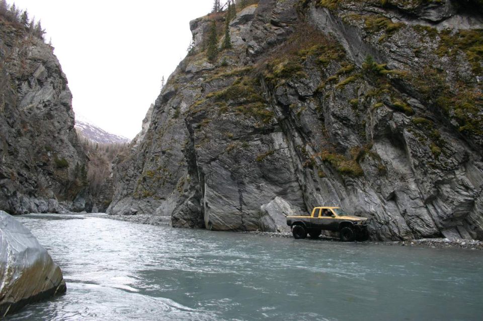 Yellow pickup truck driving in a river between rocky cliffs