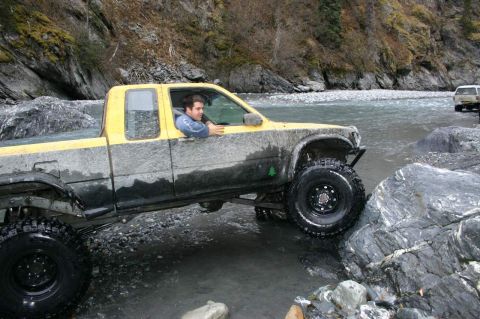 2003 Jeep TJ - Pickup truck crossing a river with rocky terrain and a second vehicle in the distance.