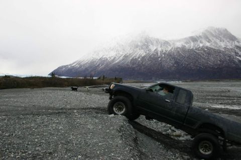 2003 Jeep TJ - A dark pickup truck navigates a , rocky landscape with a snow-covered mountain range looming in the distance.