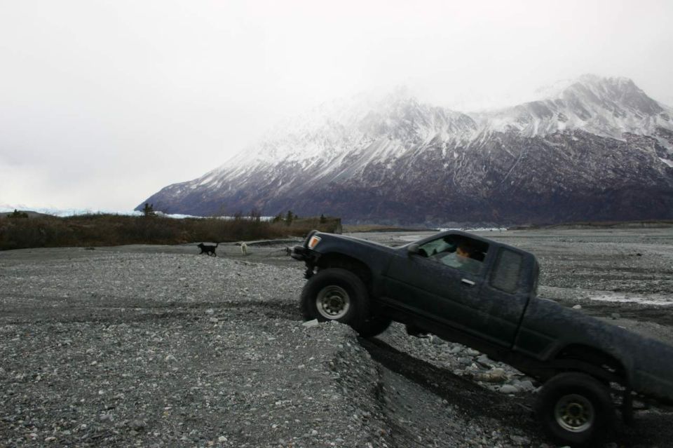 Dark pickup truck driving on a rocky, off-road terrain with a snow-capped mountain in the background