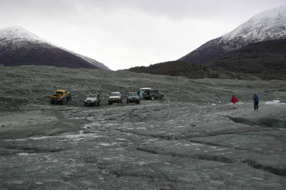Several SUVs parked on a glacier with snow-capped mountains in the background