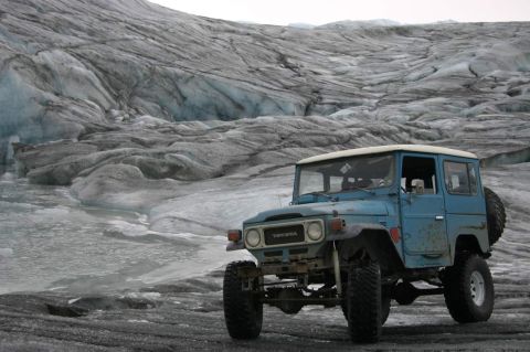 2003 Jeep TJ - A classic Toyota Land Cruiser sits before a vast, textured glacier under an overcast sky.