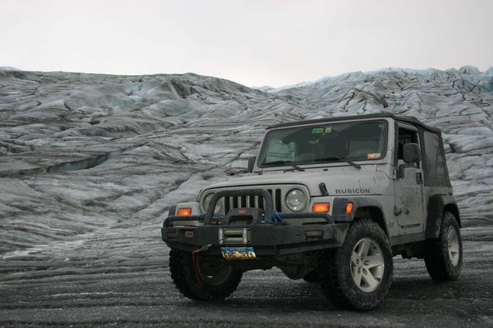 Silver Jeep Wrangler Rubicon parked on a glacier, front 3/4 view. Winch and aftermarket bumper visible