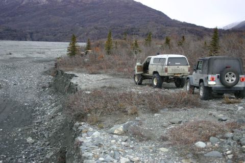 2003 Jeep TJ - Two off-road vehicles are parked on a gravelly terrain with mountains in the background.