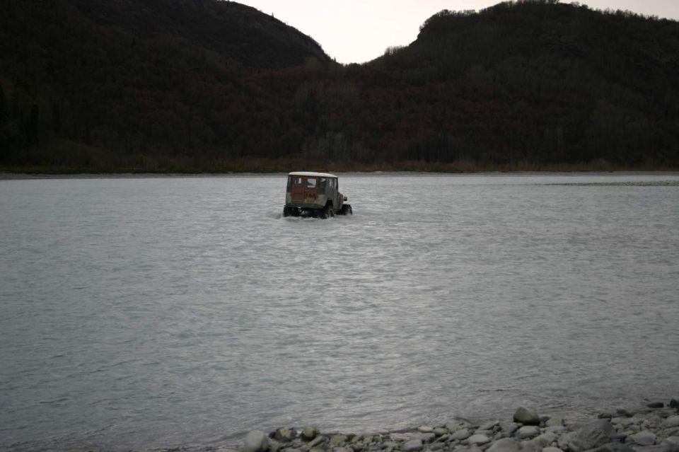 Jeep Wrangler driving through shallow river with wooded hills in background