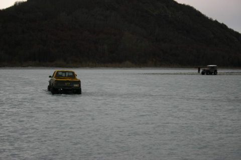 2003 Jeep TJ - A yellow pickup truck navigates through a body of water with another vehicle and a person in the background.