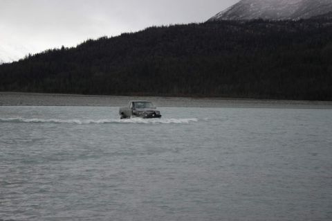 2003 Jeep TJ - A pickup truck navigates through a wide, shallow body of water with a forested mountainside in the background.
