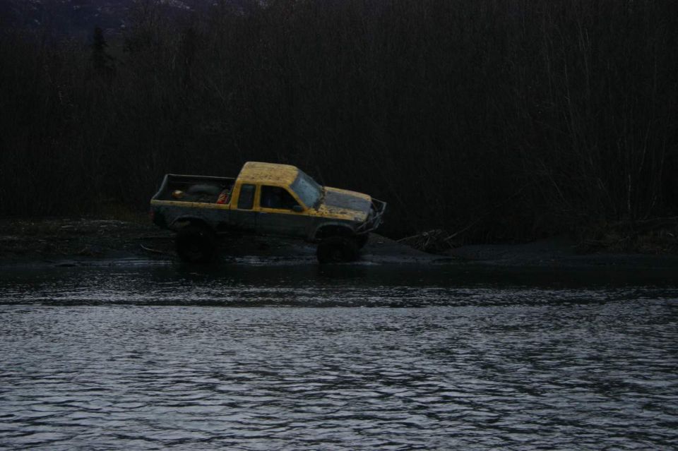 Yellow pickup truck with large tires stuck in mud near water