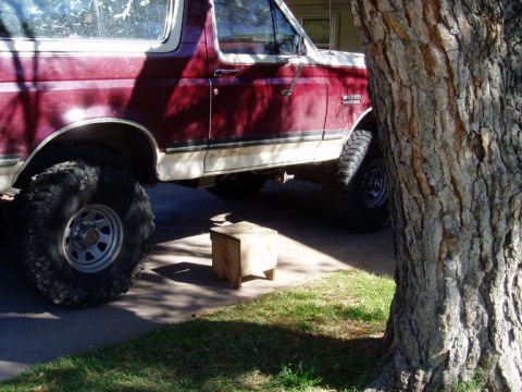 1990 Ford Bronco - A maroon and white Ford Bronco is parked outside, partially obscured by a tree.