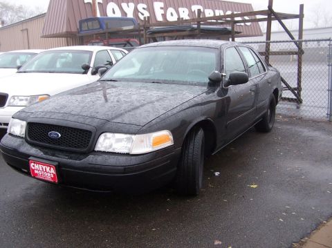 2001 Ford Crown Victoria - A black 2001 Ford Crown Victoria is parked in front of a building with other vehicles visible.