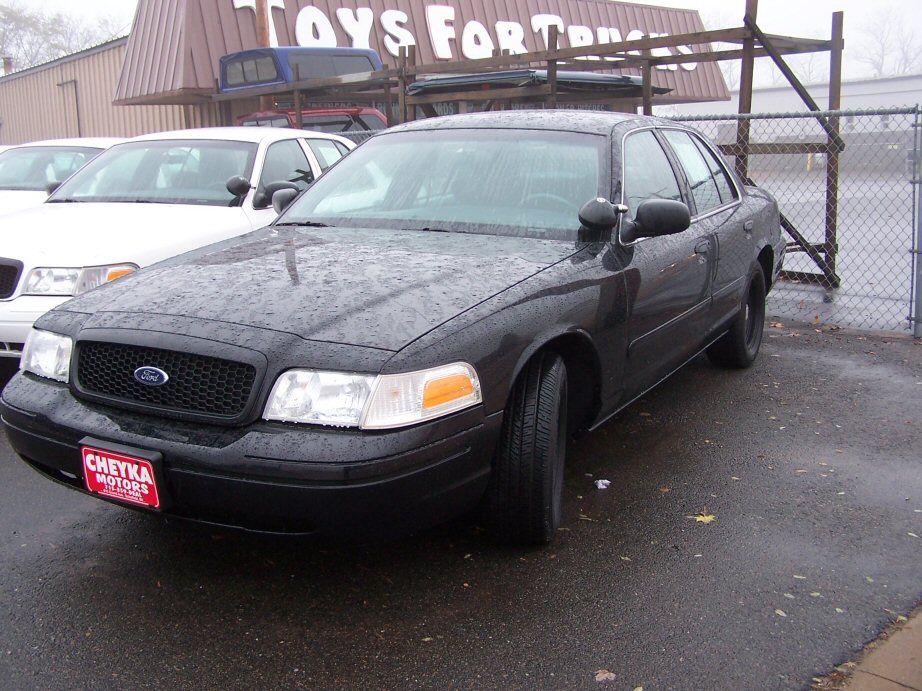 Black 2001 Ford Crown Victoria parked outside, with a white Crown Victoria behind it. Cheyka Motors plate on front