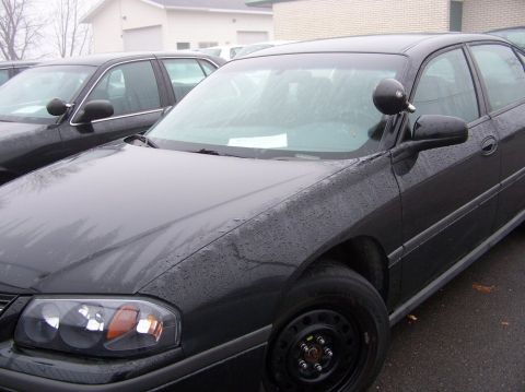2001 Ford Crown Victoria - Two dark sedans are parked outside on a wet day, one with a spotlight mounted on the side mirror.
