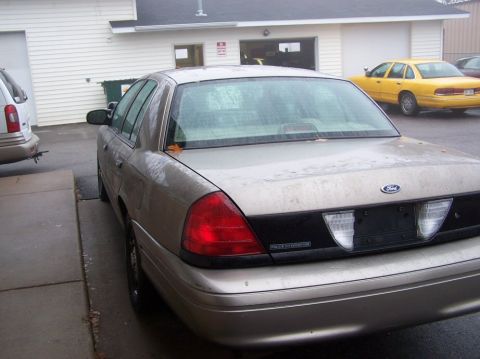 2001 Ford Crown Victoria - Tan 2001 Ford Crown Victoria parked outside a building with a yellow Ford Crown Victoria in the background.