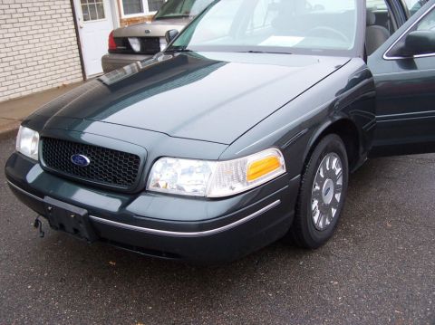 2001 Ford Crown Victoria - Front 3/4 view of a dark green 2001 Ford Crown Victoria, with the passenger door ajar and another vehicle visible in the background.