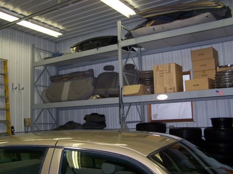2001 Ford Crown Victoria - Shelving units are filled with car parts and storage boxes, with the top of a car visible in the foreground.