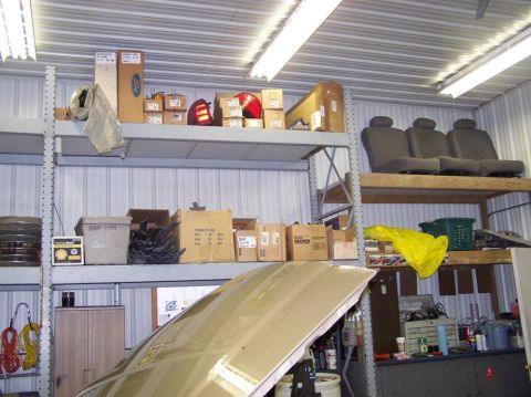 2001 Ford Crown Victoria - Shelves filled with car parts and seats are visible above an open car hood in a garage.