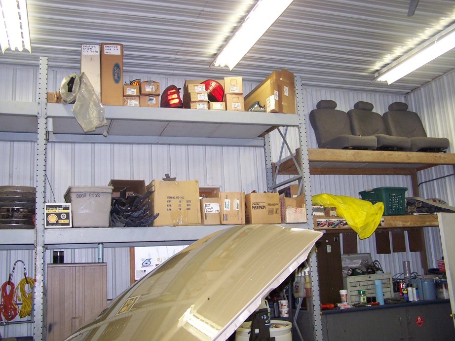Tan car hood open in garage with shelves of parts and car seats above