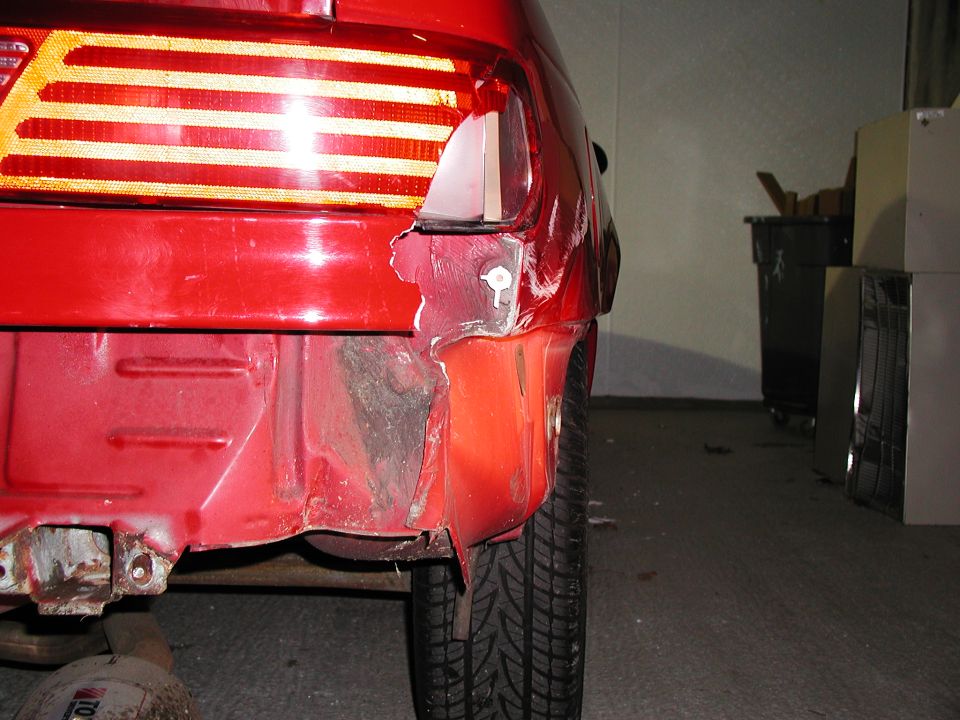 Collision damage to the red rear quarter panel of a vehicle near the taillight