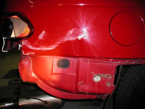 1992 Ford Taurus - The rear bumper of a red vehicle shows extensive damage, including deep scratches and a noticeable dent.