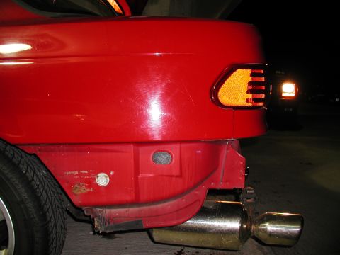 1992 Ford Taurus - The rear quarter panel and bumper of a red vehicle are visible, with a prominent taillight and exhaust pipe.