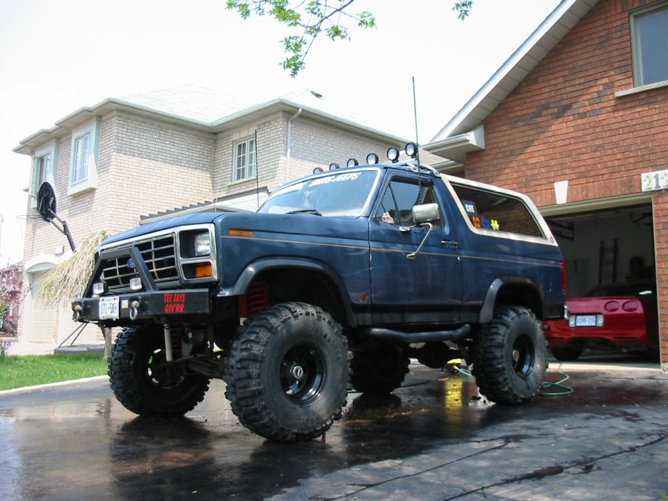 Blue 1986 Ford Bronco with large off-road tires and roof lights