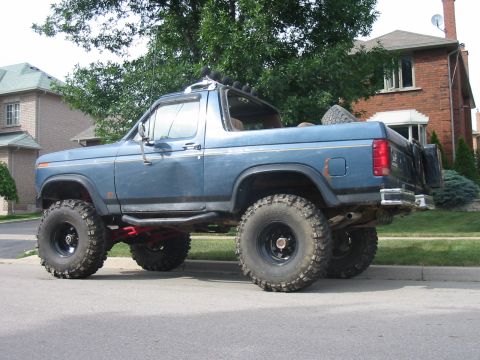 1986 Ford Bronco - Modified blue Ford Bronco parked on a suburban street, showing its lifted suspension and off-road tires.