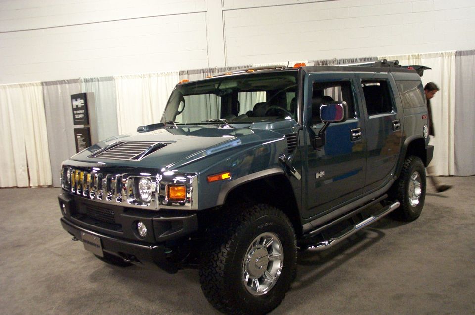 Dark green Hummer H2 SUV, front driver side view, chrome grille, aftermarket side steps, some scuffing on front bumper