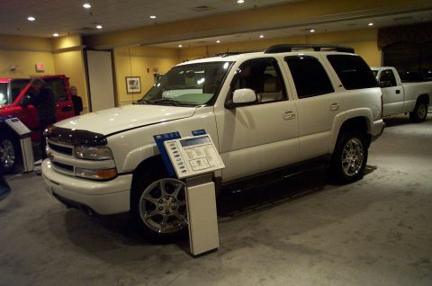 2001 Ford Crown Victoria - A white SUV is parked next to a red vehicle and a pickup truck, with a display stand in front of it.