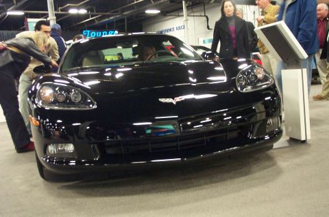 2001 Ford Crown Victoria - Black Chevrolet Corvette C6 front view at an indoor car show.