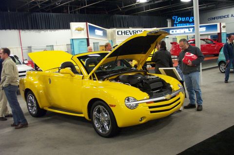 2001 Ford Crown Victoria - A yellow convertible is displayed with its hood open at an auto show.