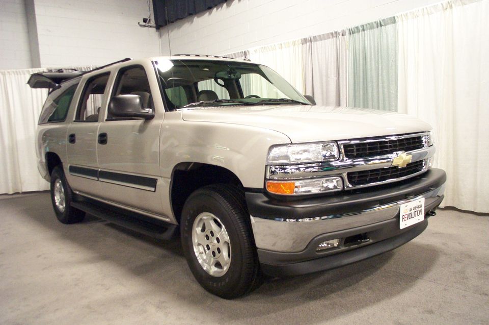 Silver SUV front 3/4 view. Grille has Chevrolet bowtie emblem. License plate reads "IN AMERICAN REVOLUTION"
